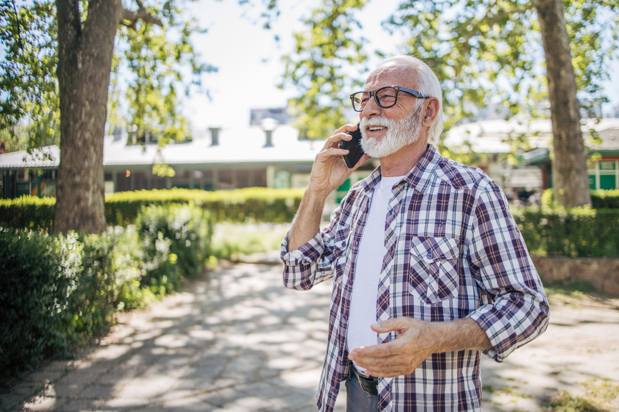 A senior man is walking in a public park in good weather and talking on his phone