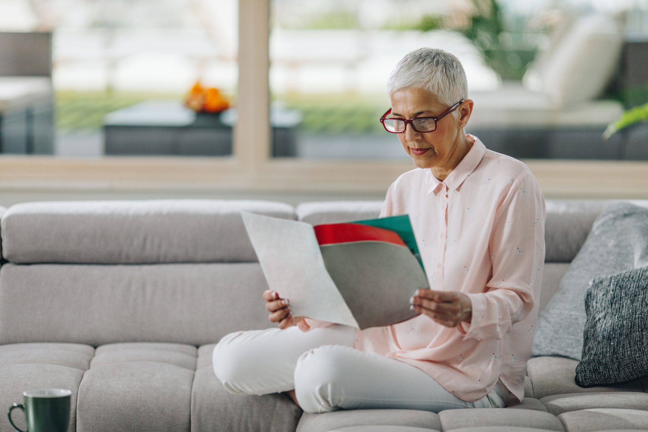 Mature woman relaxing on sofa in the living room and reading a brochure