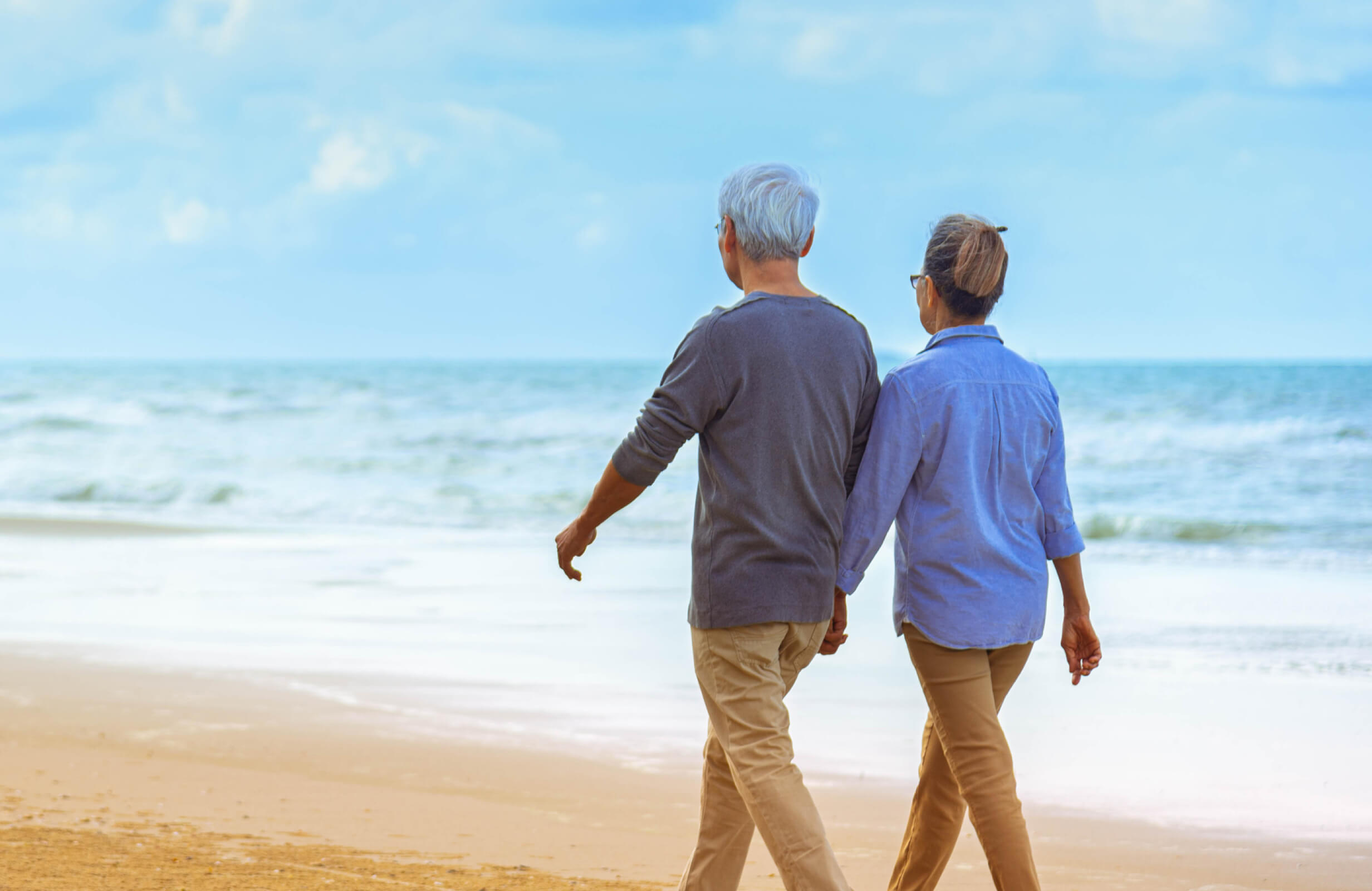 Couple walking down a beach on a sunny day holding hands.