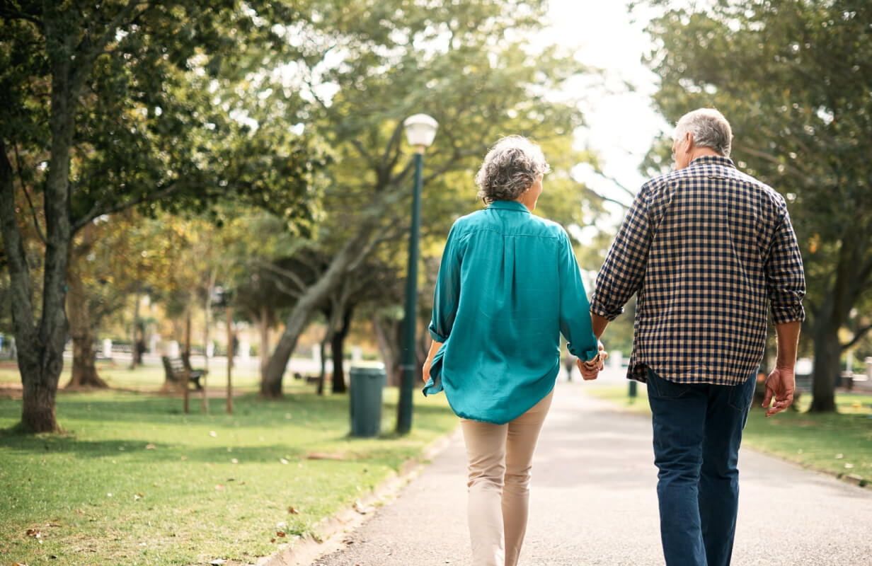 Couple walking in a sunny park holding hands.