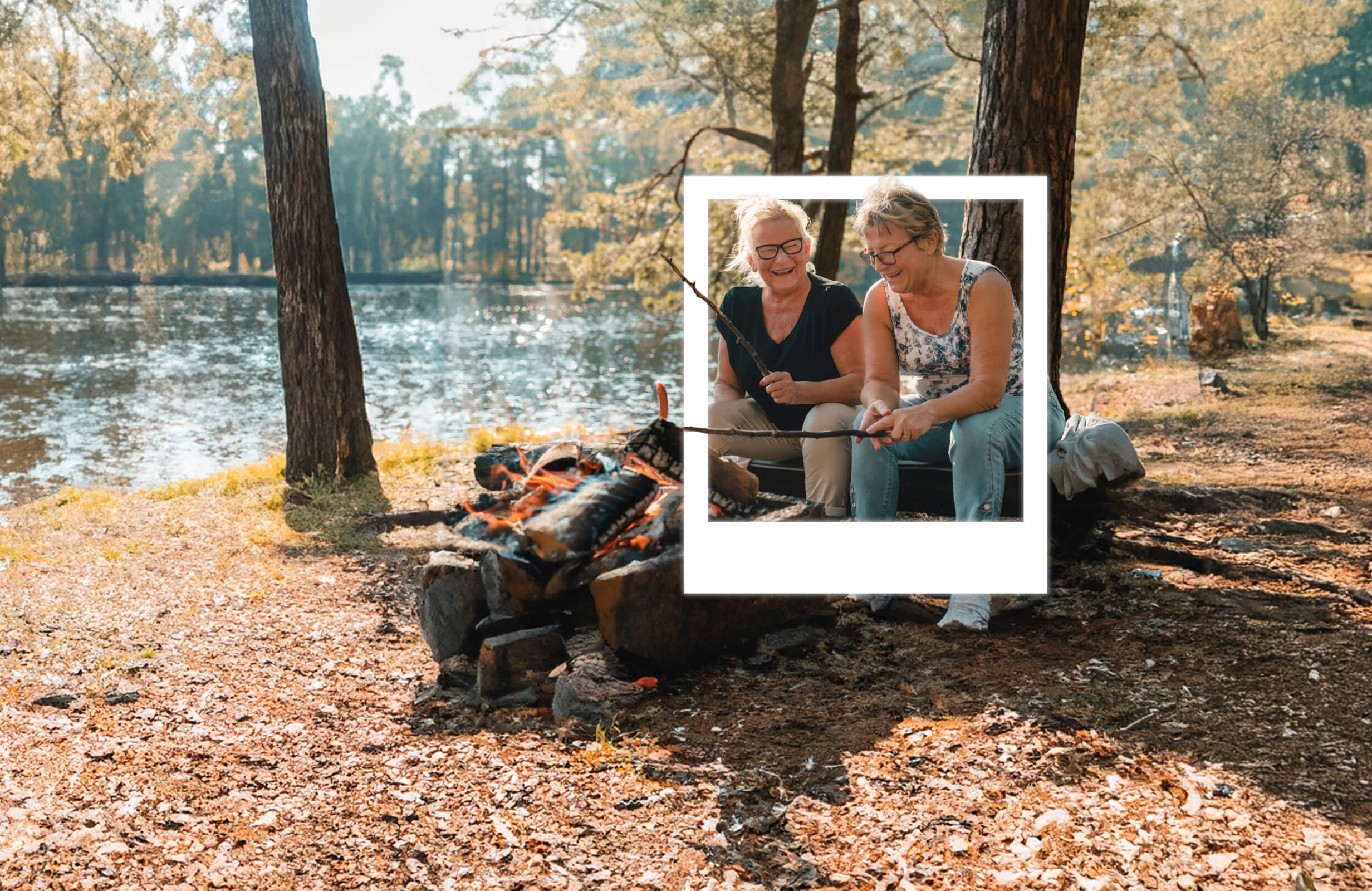 Two women sitting next to a campfire laughing and toasting marshmallows.