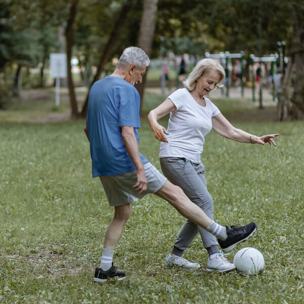 Elderly couple playing soccer in a park. 